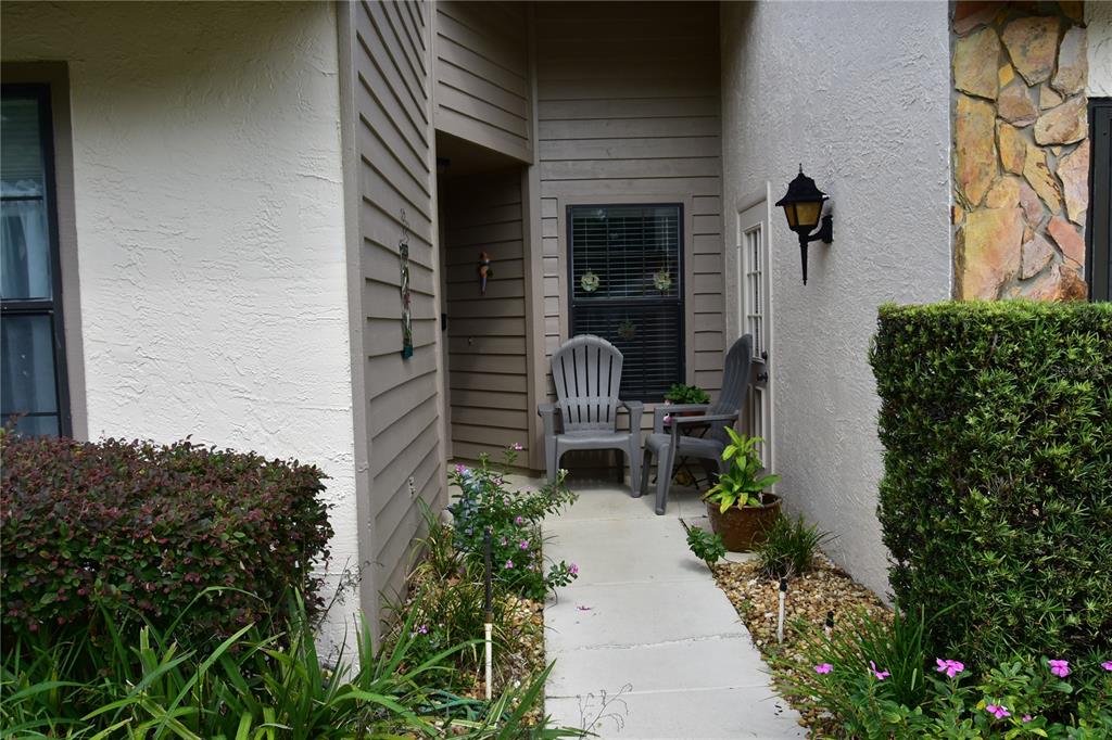 A concrete walkway leads to the front entrance of a home with two gray chairs — 2243 WYNDAM DRIVE, SPRING HILL, FL