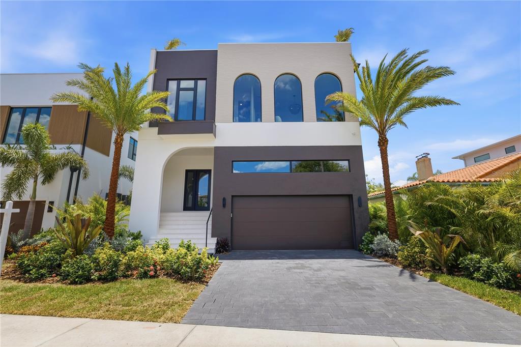 A modern two-story house features a dark garage, arched windows, and palm trees in front — 128 ADRIATIC AVENUE, TAMPA, FL