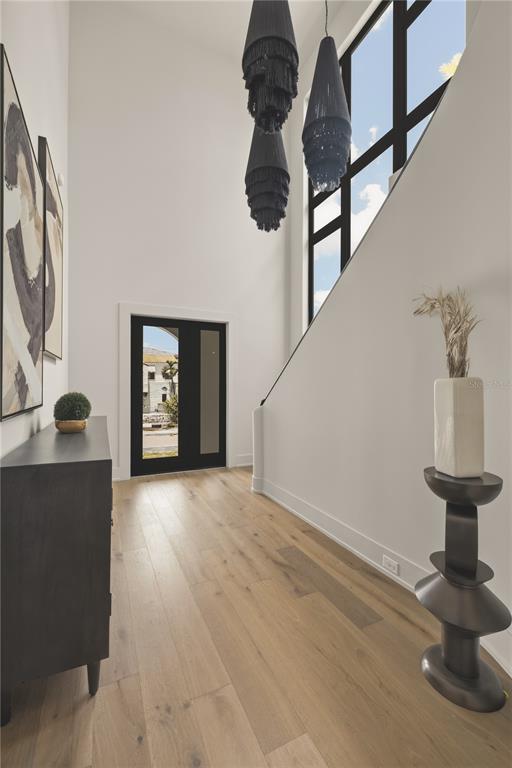 A bright entryway features light wood floors, a tall window, and a modern tiered chandelier — 128 ADRIATIC AVENUE, TAMPA, FL