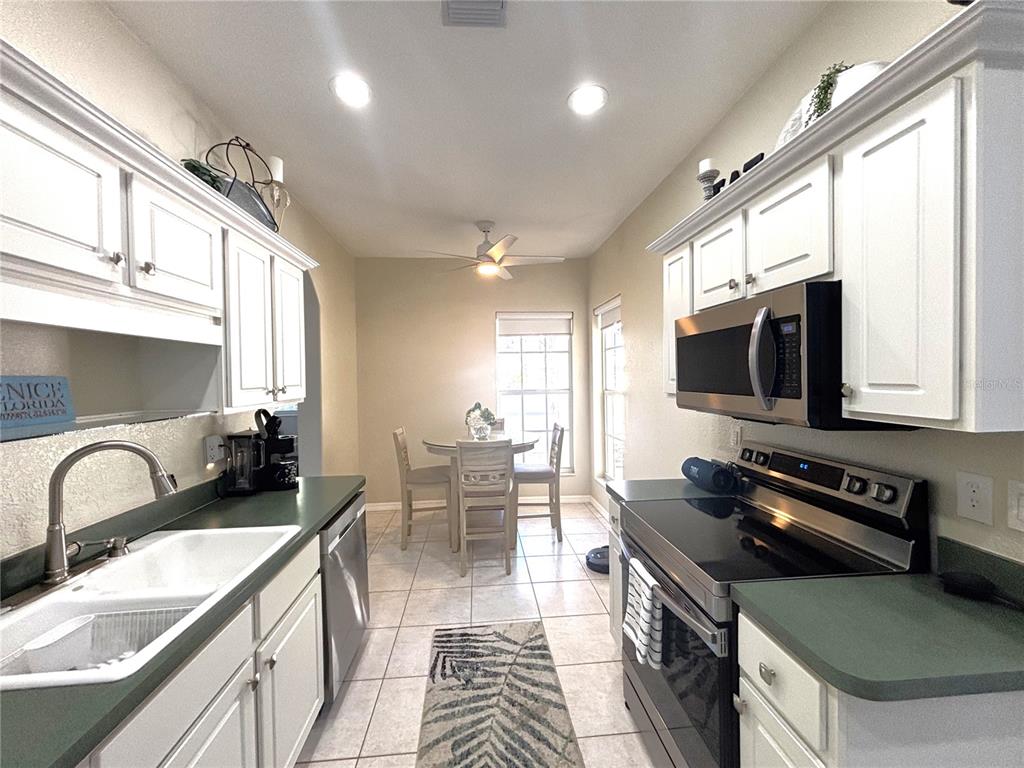 A kitchen with white cabinets, green countertops, and a dining area with a round table — 1759 FOUNTAIN VIEW CIRCLE UNIT 1759, VENICE, FL
