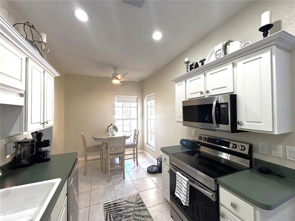 A kitchen with white cabinets, green countertops, stainless steel appliances, and a small dining area — 1759 FOUNTAIN VIEW CIRCLE UNIT 1759, VENICE, FL