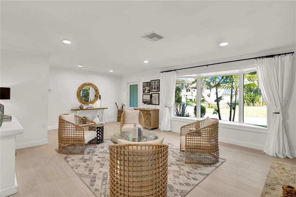 A bright living room features light wood floors, woven armchairs, and a large bay window — 1945 ANGLERS COVE, VERO BEACH, FL
