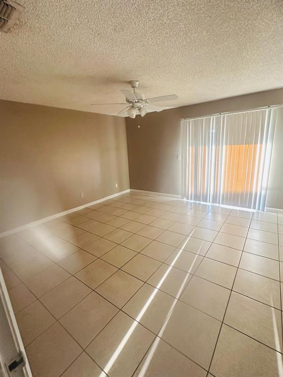 An empty room with beige tile flooring, tan walls, a ceiling fan, and vertical blinds — 502 WINTER TERRACE UNIT 121, WINTER HAVEN, FL