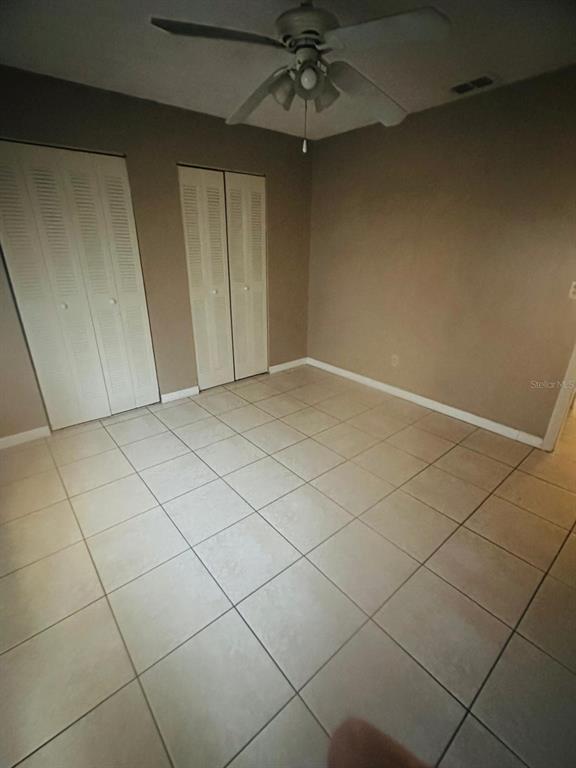 An empty bedroom features light-colored tile flooring, beige walls, and two white louvered closet doors — 502 WINTER TERRACE UNIT 121, WINTER HAVEN, FL