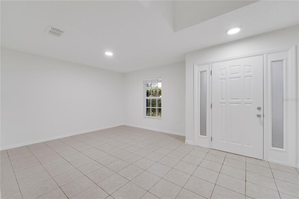 An empty room with white walls, tiled flooring, a single window, and a front door — 13403 COPPER HEAD DRIVE, RIVERVIEW, FL