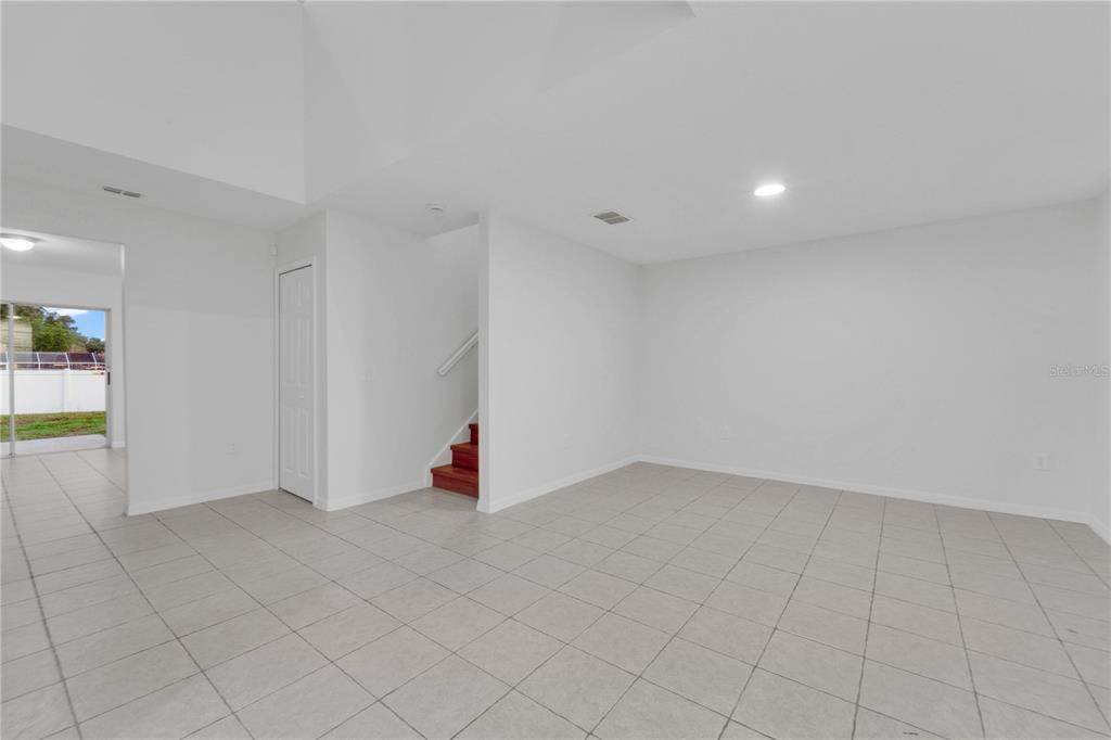 A bright, empty room features white walls, light-colored tile flooring, and a staircase with red steps — 13403 COPPER HEAD DRIVE, RIVERVIEW, FL