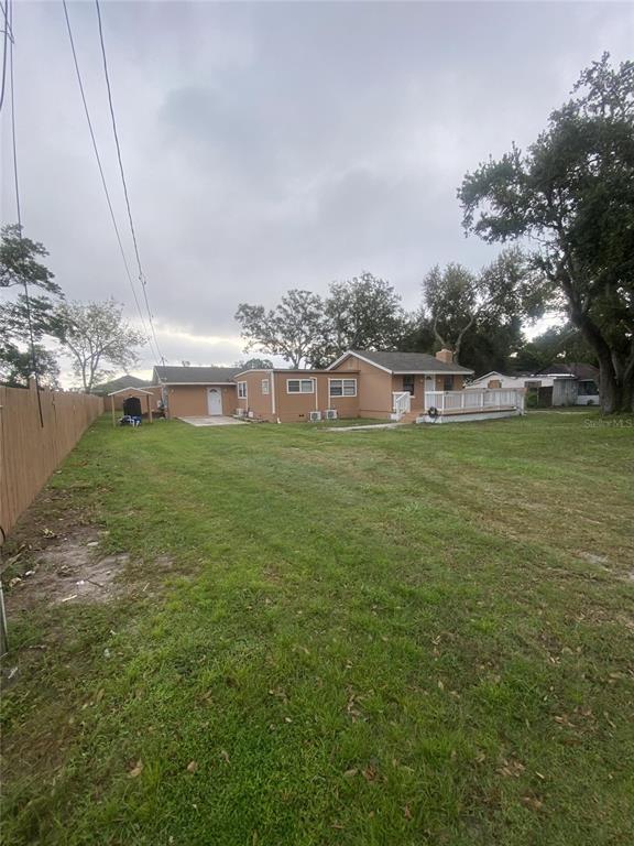 A tan house with a wooden deck and a large grassy backyard under a cloudy sky — 1801 DANIELS STREET, KISSIMMEE, FL