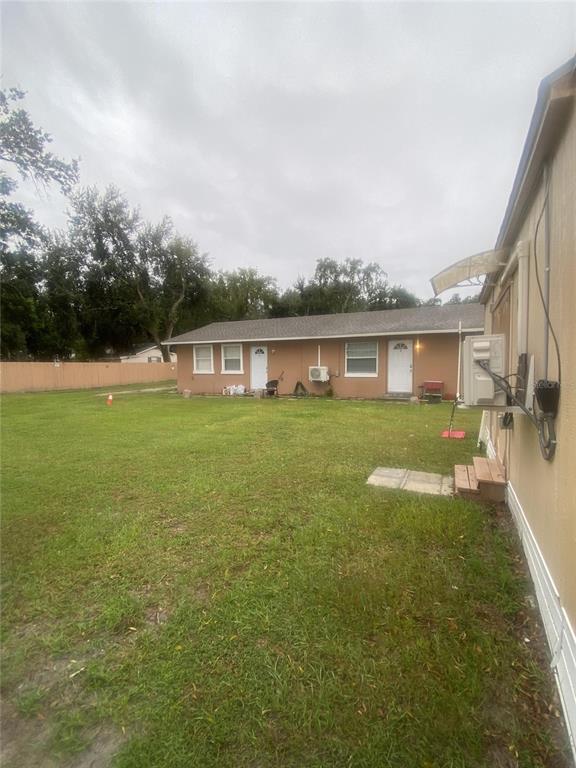 A view of a grassy backyard facing a single-story duplex with two white entry doors — 1801 DANIELS STREET, KISSIMMEE, FL