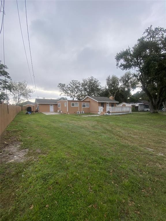 A tan house with a wooden deck and a large grassy yard under a cloudy sky — 1801 DANIELS STREET, KISSIMMEE, FL
