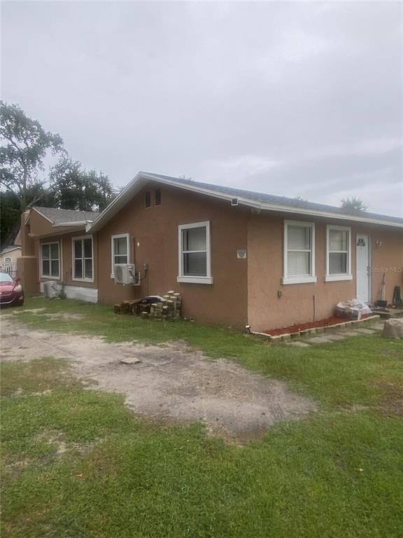 A tan, single-story house with a white door and several windows sits on a grassy lot — 1801 DANIELS STREET, KISSIMMEE, FL