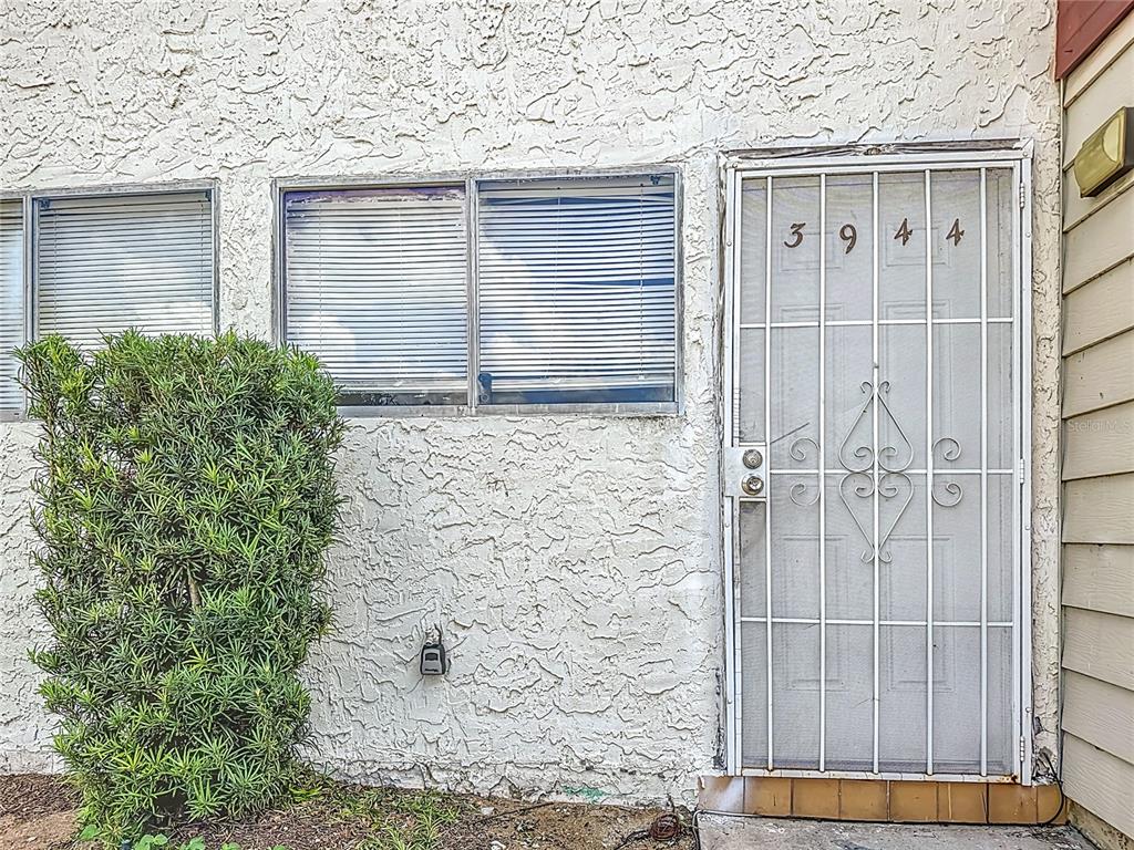 A white stucco exterior wall features two windows with blinds and a metal security door — 3944 CRAYRICH CIRCLE UNIT A-4, ORLANDO, FL