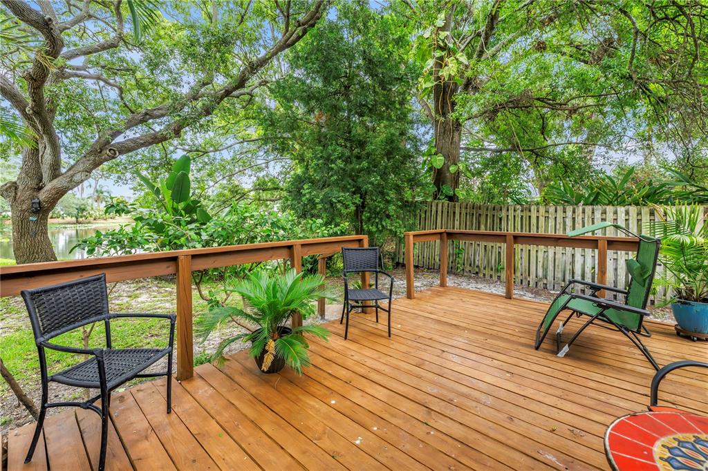 A wooden deck features patio furniture, potted plants, and a view of trees and water — 10495 LONGWOOD DRIVE, SEMINOLE, FL