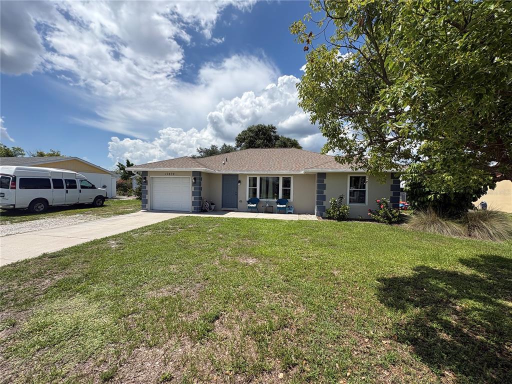 A single-story house with a tan exterior, a white garage door, and a large front lawn — 13476 ROMFORD AVENUE, PORT CHARLOTTE, FL
