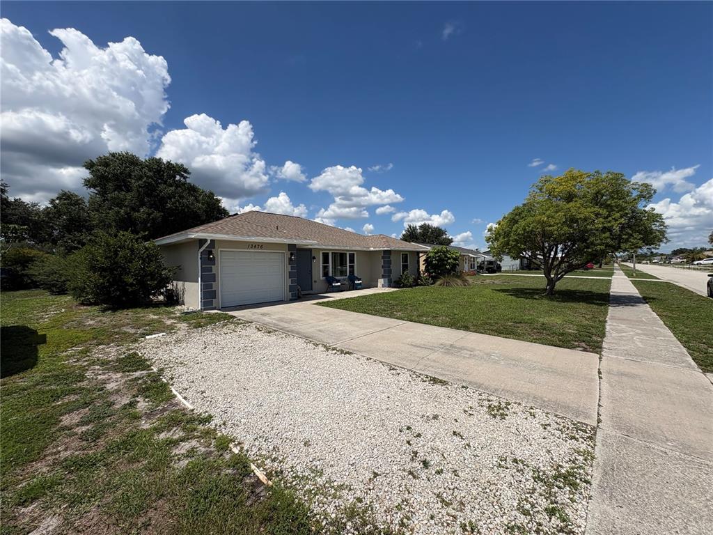 A single-story house with a white garage, concrete driveway, and a gravel parking area — 13476 ROMFORD AVENUE, PORT CHARLOTTE, FL