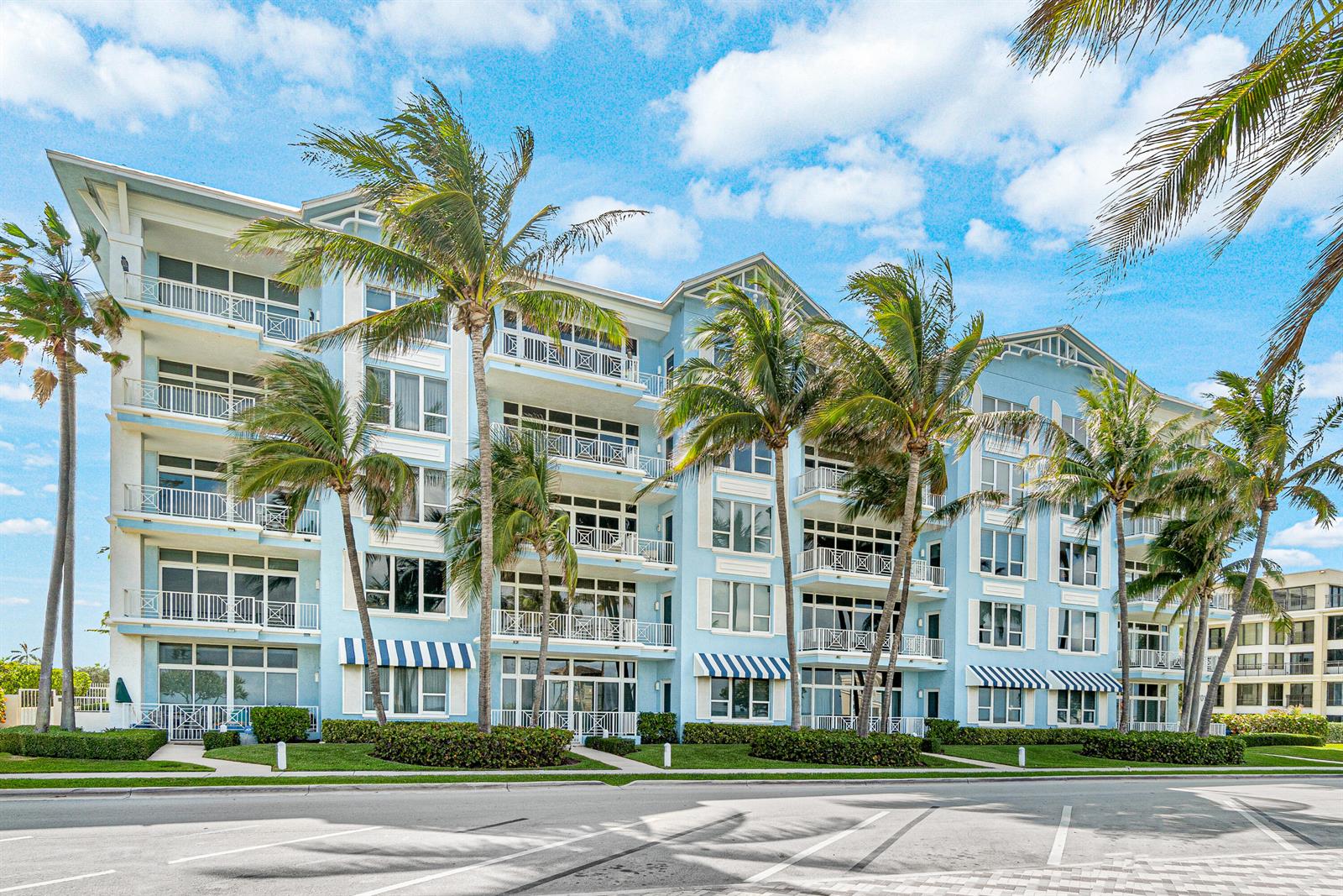 A multi-story light blue apartment building features balconies, striped awnings, and surrounding palm trees — 701 SE 21st Avenue # 301, Deerfield Beach FL 33441, DEERFIELD BEACH, FL