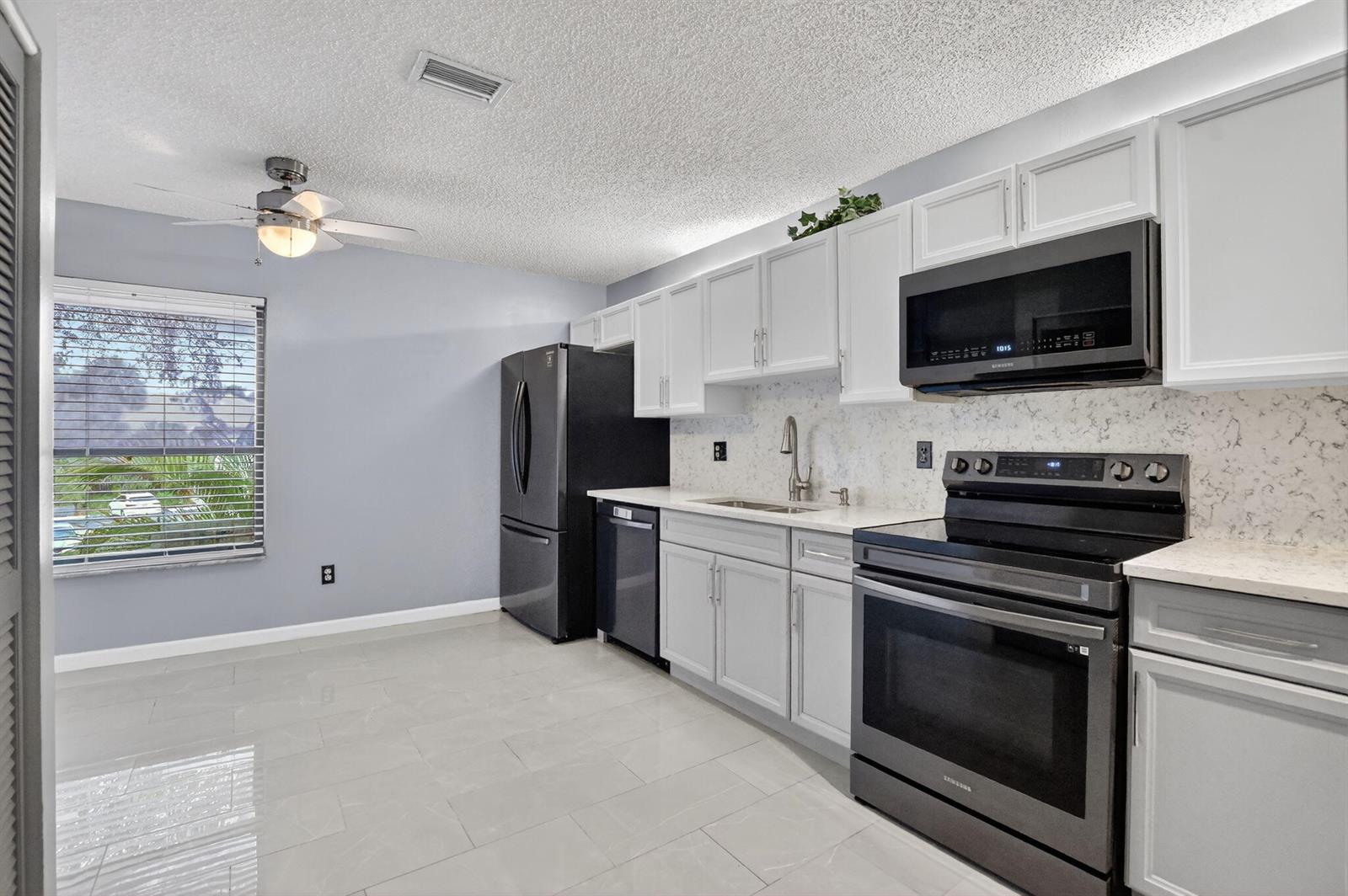 A kitchen with white cabinets, black appliances, quartz countertops, and light gray tile flooring — 9364 Sable Ridge Circle # B, Boca Raton FL 33428, BOCA RATON, FL