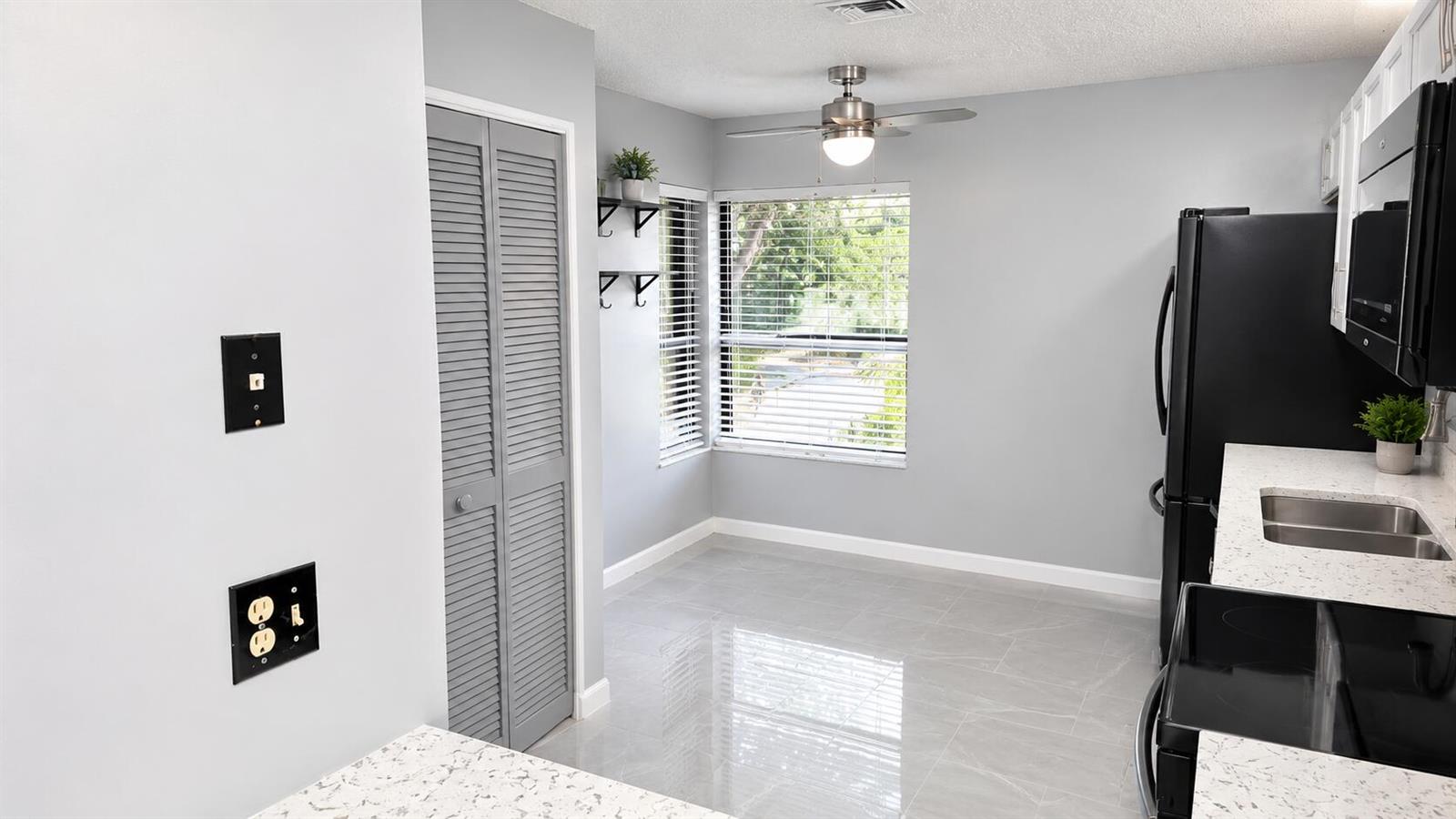 A kitchen with gray walls, white speckled countertops, black appliances, and a windowed dining area — 9364 Sable Ridge Circle # B, Boca Raton FL 33428, BOCA RATON, FL