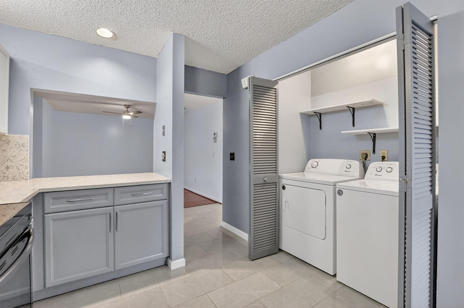A laundry area with white appliances and gray cabinets sits next to a kitchen counter — 9364 Sable Ridge Circle # B, Boca Raton FL 33428, BOCA RATON, FL