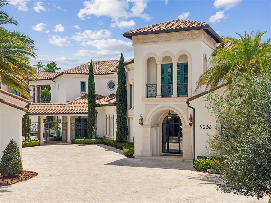 A Mediterranean-style house features a tiled roof, a stone-arched entryway, and a paved driveway — 9236 BAY POINT DRIVE, ORLANDO, FL