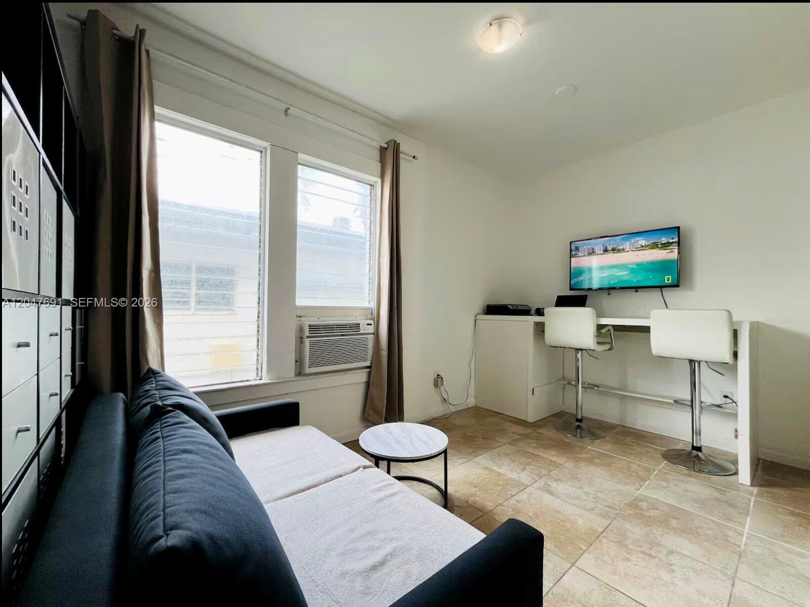 A room with a sofa, a desk with two stools, a wall-mounted television, and tile flooring — 842 Meridian # 2F, Miami Beach FL 33139, MIAMI BEACH, FL