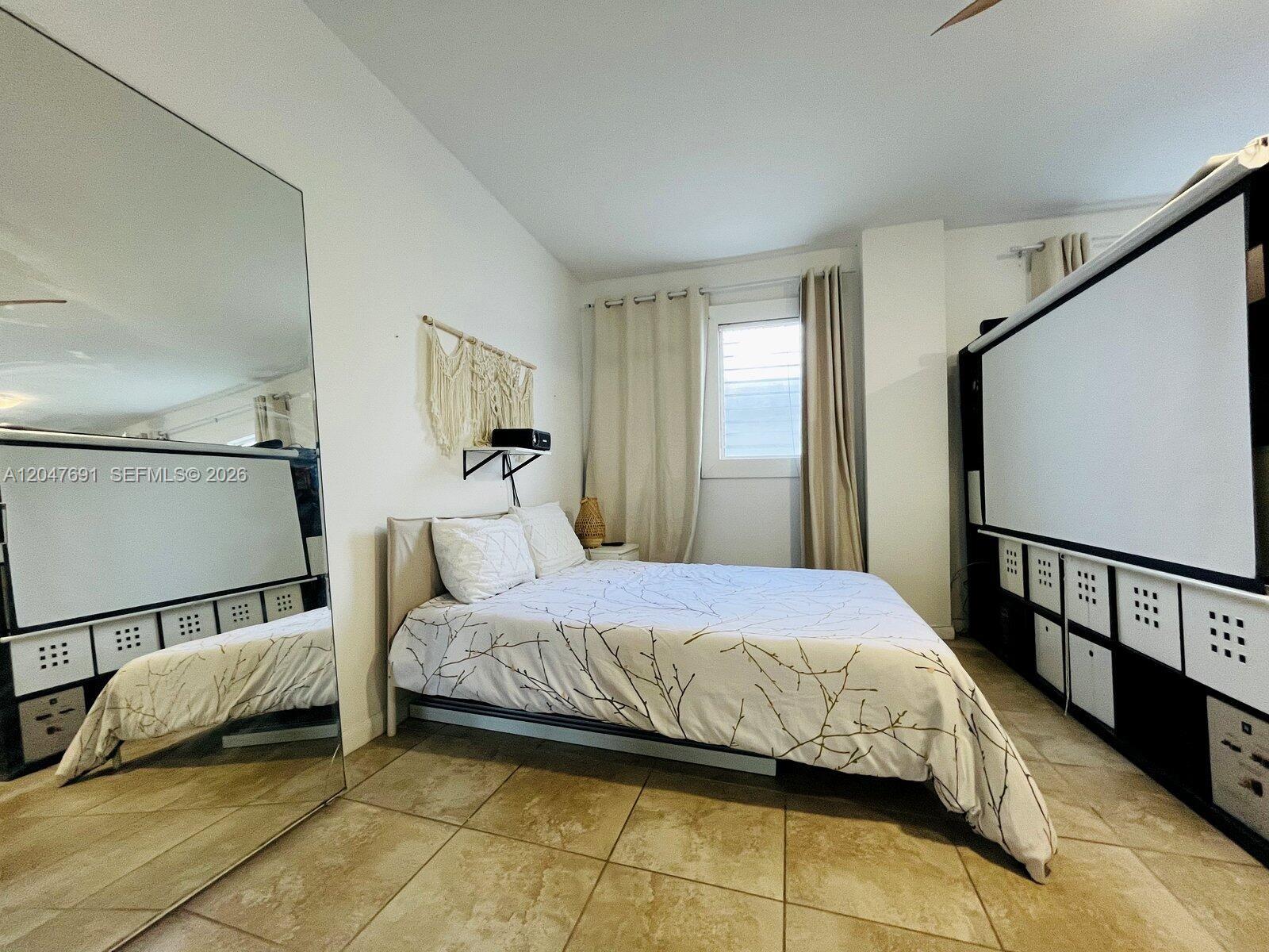 A bedroom features a bed, a large wall mirror, and a projector screen with storage — 842 Meridian # 2F, Miami Beach FL 33139, MIAMI BEACH, FL