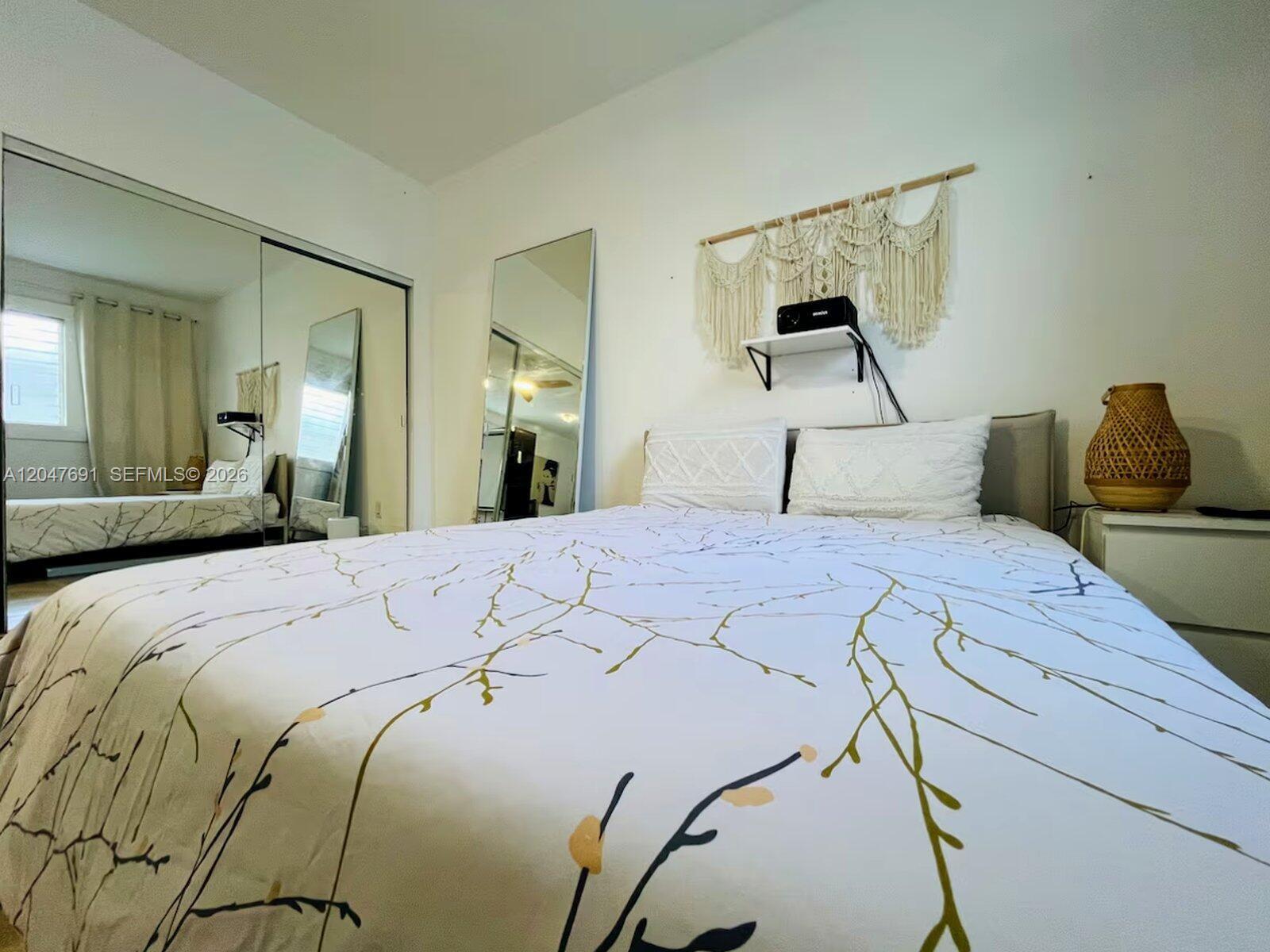 A bedroom features a bed with a branch-patterned duvet, mirrored closet doors, and wall decor — 842 Meridian # 2F, Miami Beach FL 33139, MIAMI BEACH, FL