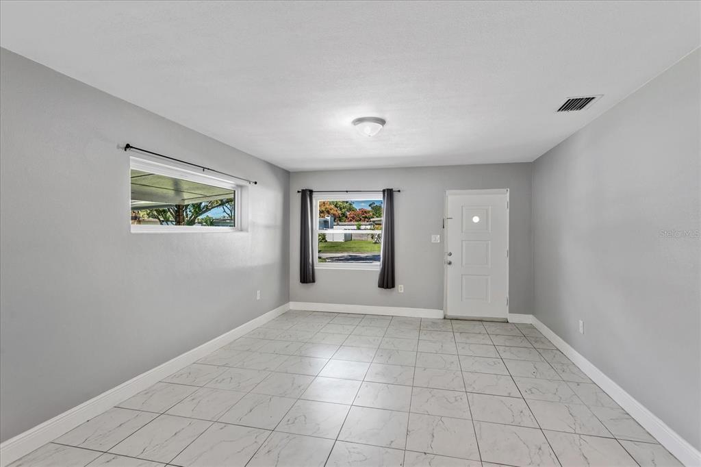 A bright, empty room features gray walls, white tile flooring, and a white entry door — 3522 PRICE AVENUE, ORLANDO, FL