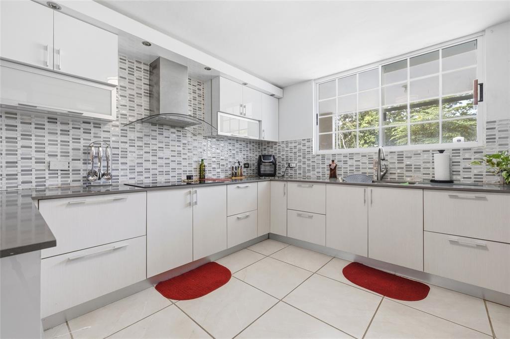 A modern kitchen features white cabinetry, gray countertops, a tiled backsplash, and light floor tiles — 29 Calle 1 URB. SAN RAFAEL ESTATES, TRUJILLO ALTO, PR