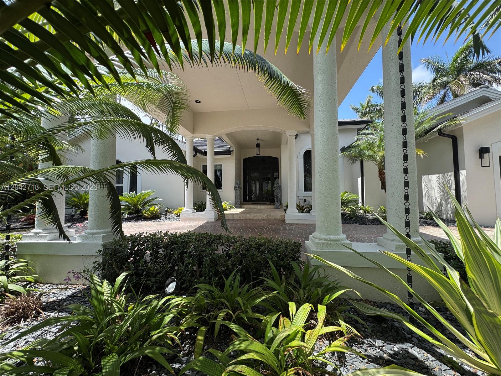 A covered entryway features white columns, a brick floor, and lush tropical landscaping — 9662 SW 123rd St, Miami FL 33176, MIAMI, FL