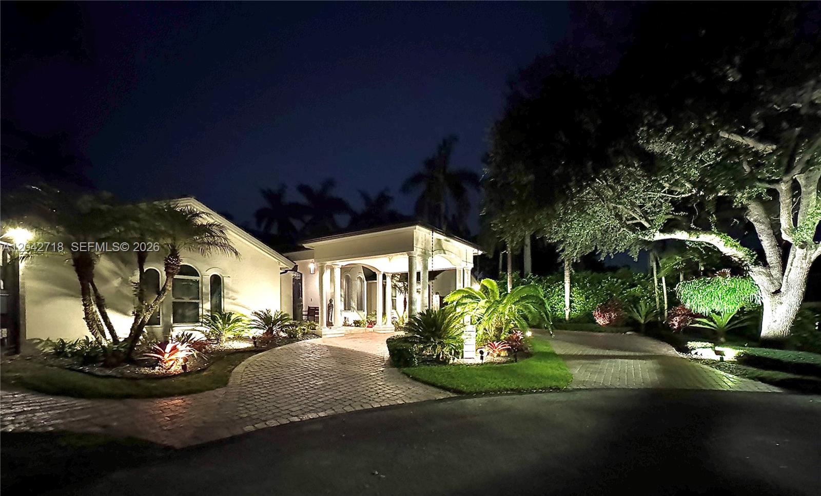 A night view shows a house exterior with a paved driveway and illuminated landscaping — 9662 SW 123rd St, Miami FL 33176, MIAMI, FL