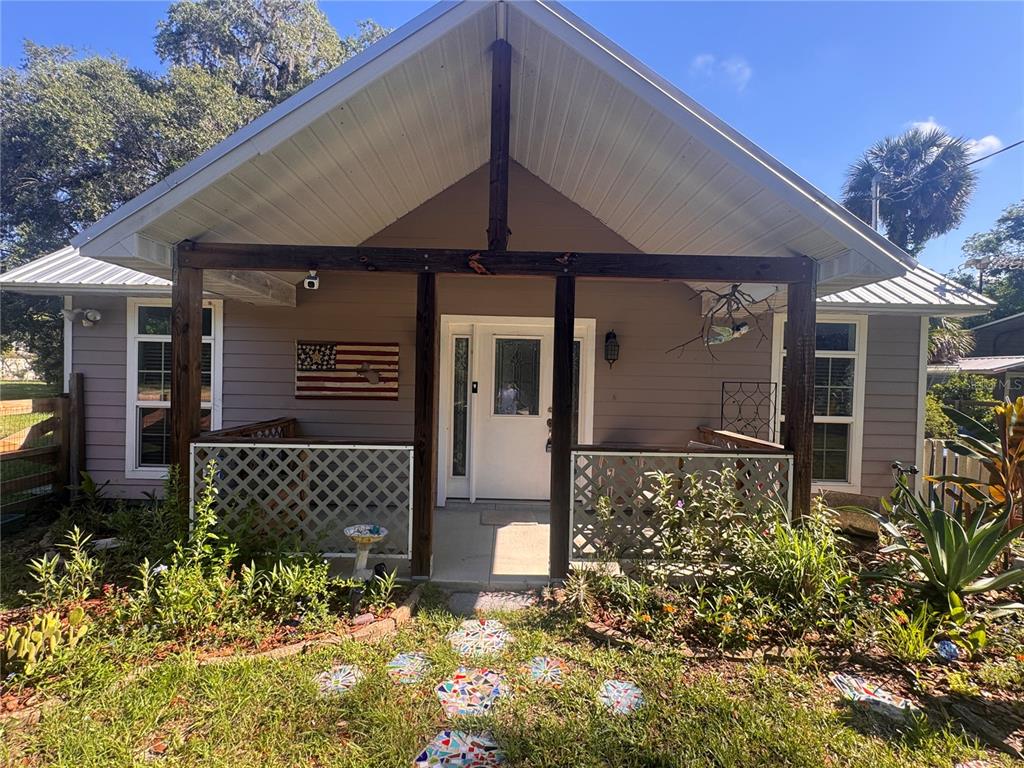 A single-story house features a covered front porch with lattice railings and a metal roof — 103 GROVE STREET, MELROSE, FL