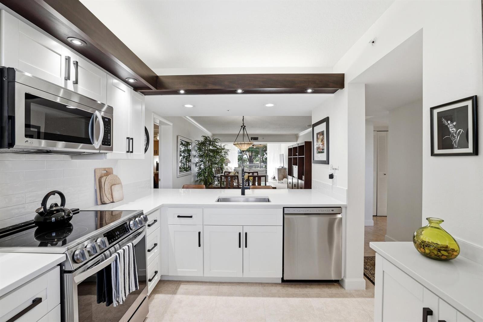 A modern kitchen features white cabinets, stainless steel appliances, and a dark wood ceiling beam — 2101 Marina Isle Way # 404, Jupiter FL 33477, JUPITER, FL