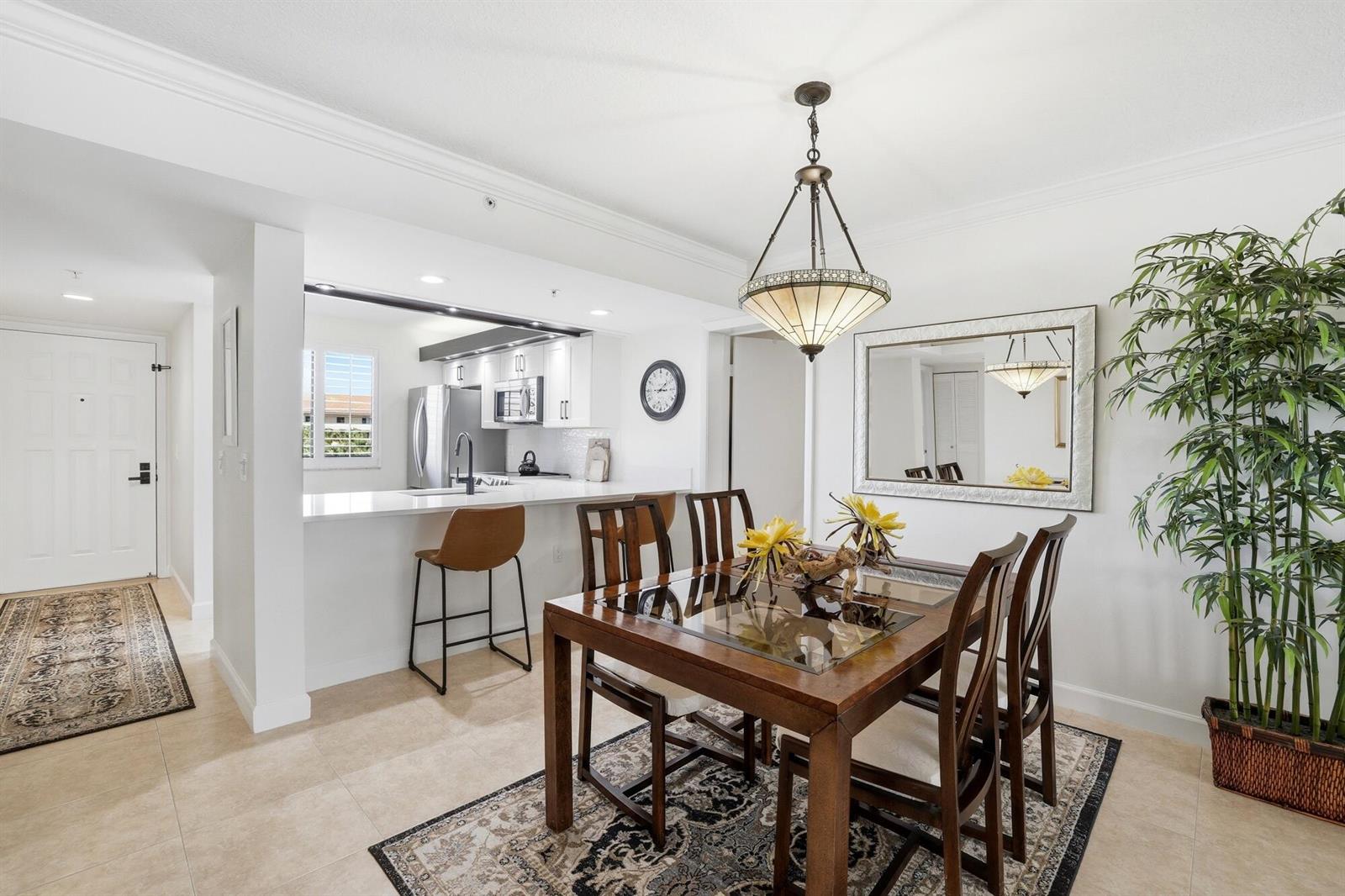 A dining area with a glass-topped wooden table sits adjacent to an open-concept kitchen — 2101 Marina Isle Way # 404, Jupiter FL 33477, JUPITER, FL