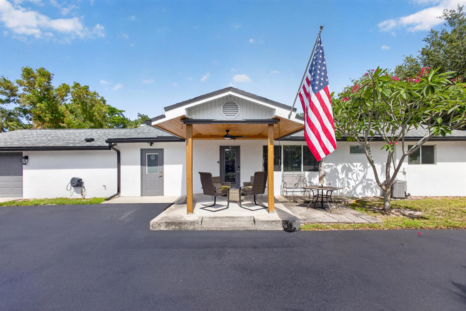 A white house with a covered front porch, a large American flag, and asphalt driveway — 5500 West Place, Mangonia Park FL 33407, MANGONIA PARK, FL