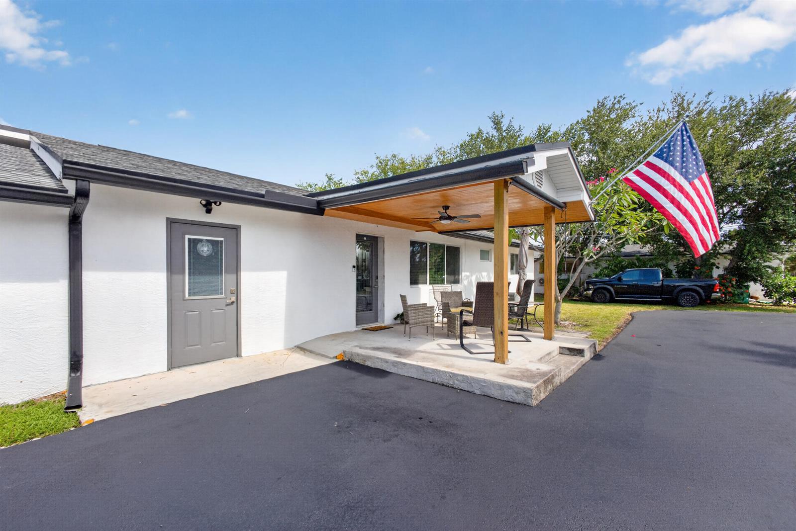 A white house exterior features a covered patio with a wooden ceiling and a driveway — 5500 West Place, Mangonia Park FL 33407, MANGONIA PARK, FL