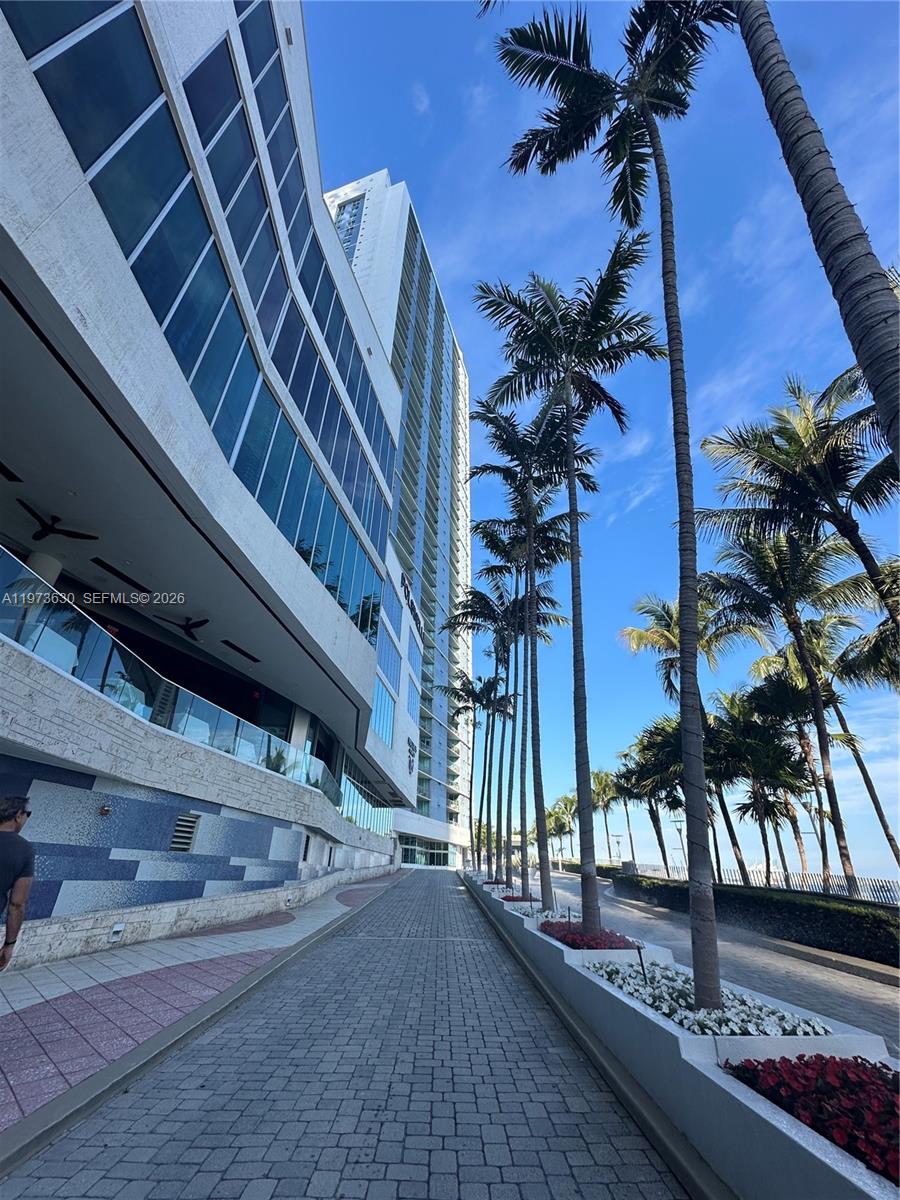 A paved walkway leads toward a tall modern building lined with palm trees — 335 S Biscayne Blvd # 1002, Miami FL 33131, MIAMI, FL