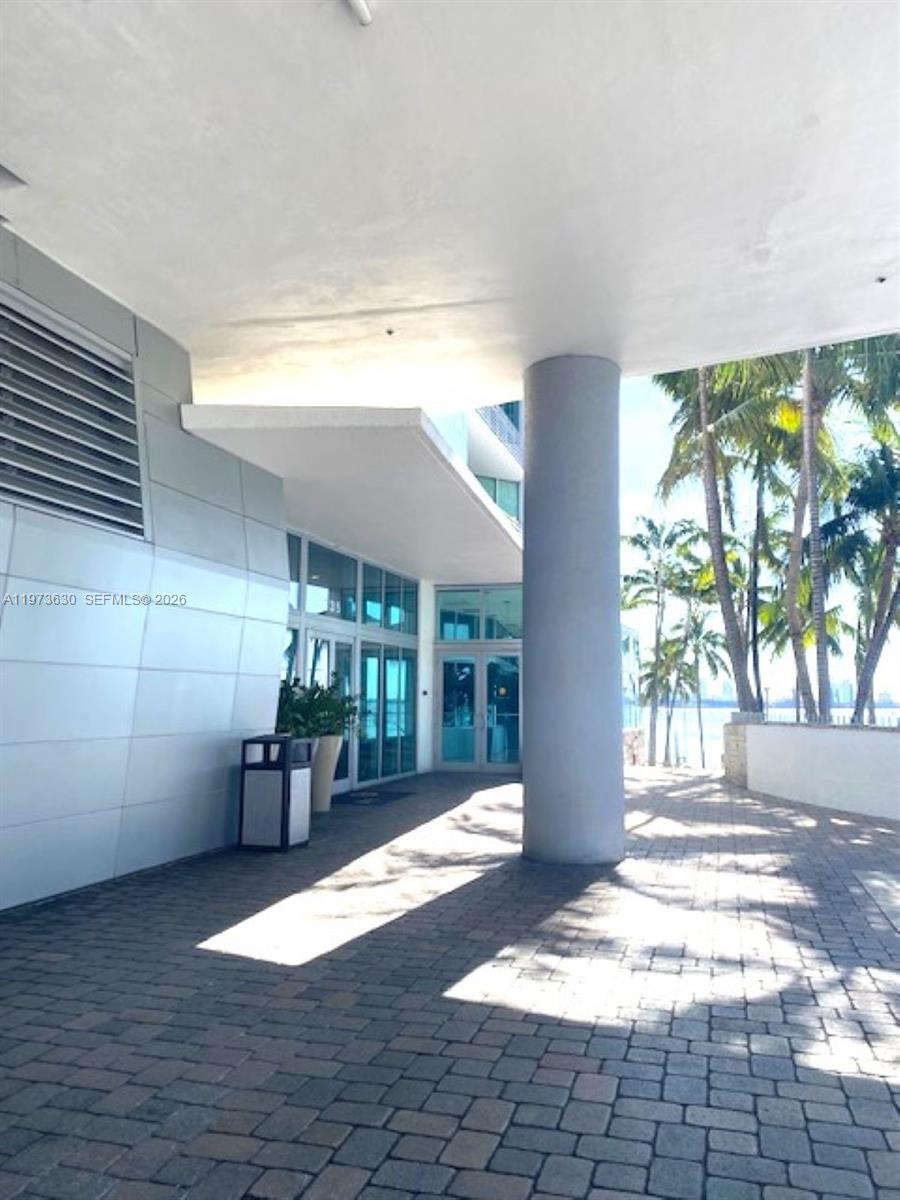 A paved walkway leads to a building entrance with glass doors and a large pillar — 335 S Biscayne Blvd # 1002, Miami FL 33131, MIAMI, FL
