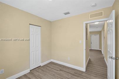 An empty room with beige walls, light wood-look flooring, and a white closet door — POMPANO BEACH, FL