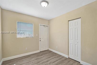 An empty room with light-colored walls, wood-look flooring, a window, a door, and a closet — POMPANO BEACH, FL