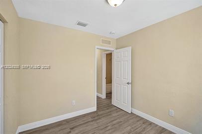 An empty room with beige walls, wood-look flooring, and a white interior door — POMPANO BEACH, FL