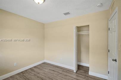 A bedroom with light-colored walls, wood-look flooring, a ceiling light, and an open closet — POMPANO BEACH, FL