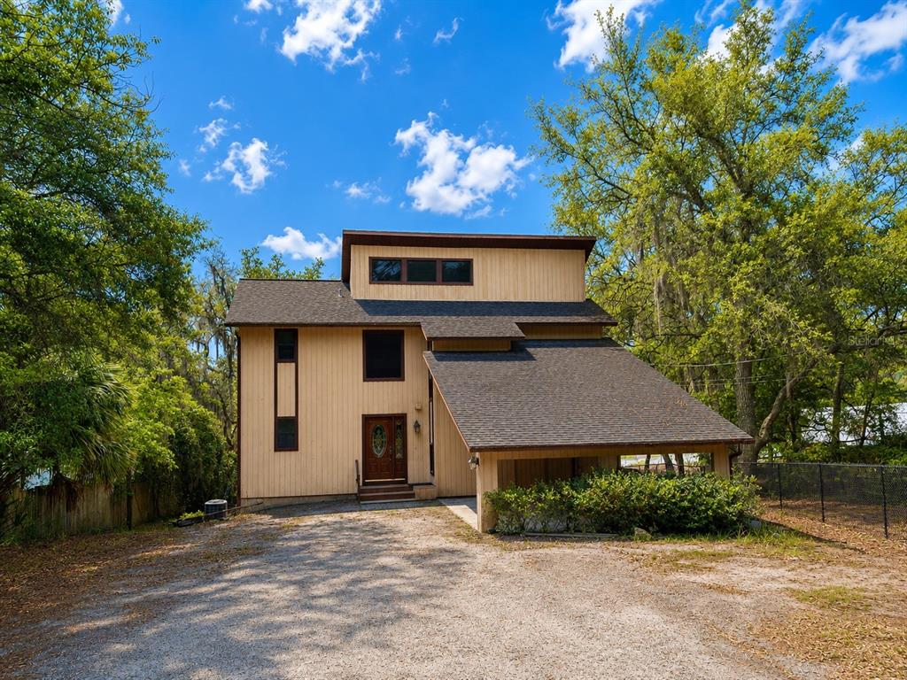 A two-story house with tan vertical siding, a dark shingled roof, and a gravel driveway — 7119 IMMOKALEE ROAD, KEYSTONE HEIGHTS, FL