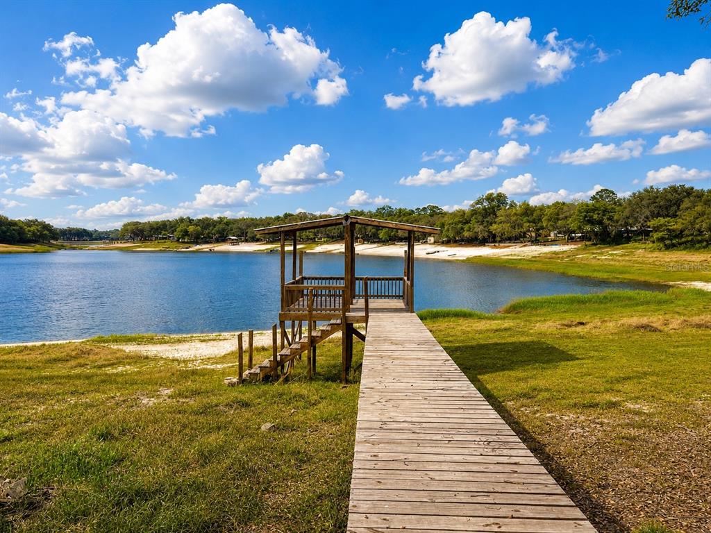 A wooden dock with a covered gazebo extends into a lake under a blue sky — 7119 IMMOKALEE ROAD, KEYSTONE HEIGHTS, FL