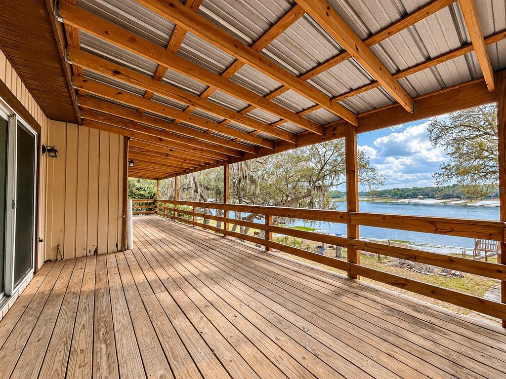 A wide wooden deck with a metal roof overlooks a lake with trees — 7119 IMMOKALEE ROAD, KEYSTONE HEIGHTS, FL
