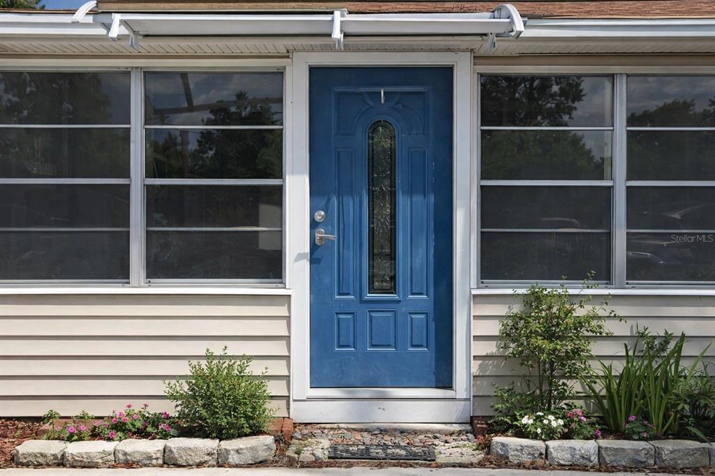 A blue front door is centered between two large windows on a light-colored siding exterior — 408 LONGFELLOW BOULEVARD, LAKELAND, FL