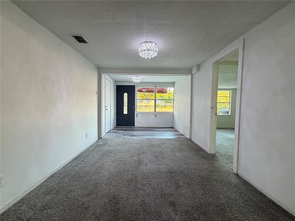 A living room with gray carpet leads to an entryway with a dark front door — 408 LONGFELLOW BOULEVARD, LAKELAND, FL