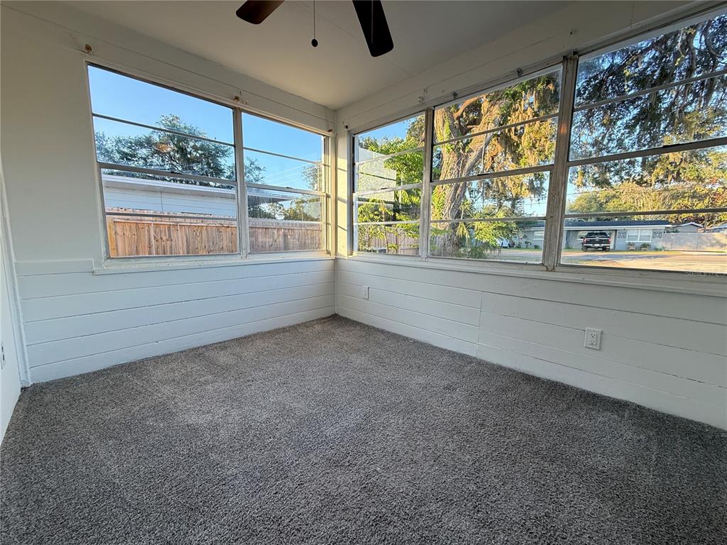 A sunroom features gray carpeting, white horizontal wood paneling, and large windows overlooking a yard — 408 LONGFELLOW BOULEVARD, LAKELAND, FL