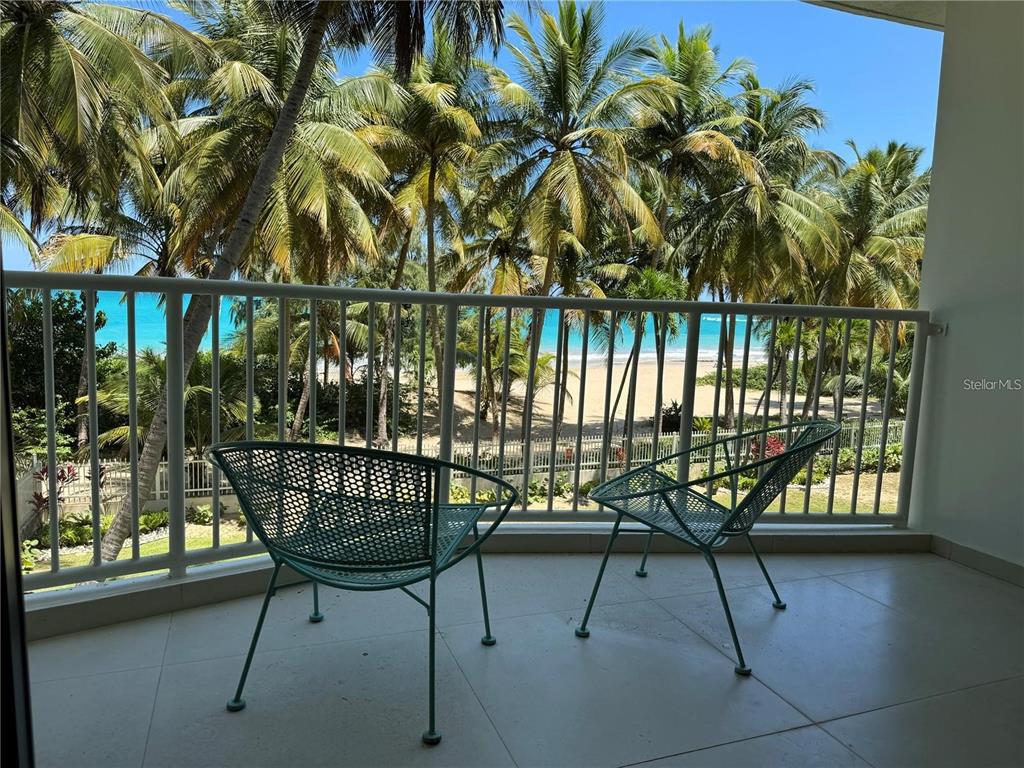 A balcony with two green metal chairs overlooks a sandy beach and palm trees — 4633 AVE ISLA VERDE UNIT L202, CAROLINA, PR