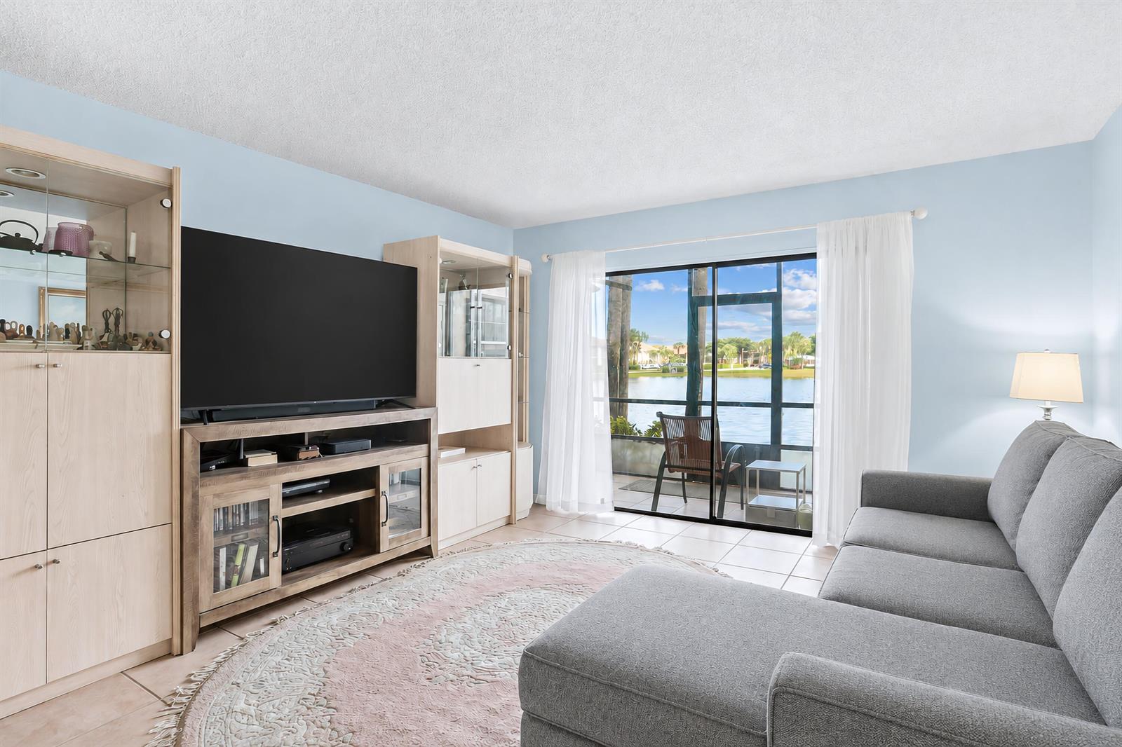 A living room features a grey sectional sofa, entertainment center, and sliding doors overlooking water — 7892 Willow Springs Drive # 1517, FL 33467, FL