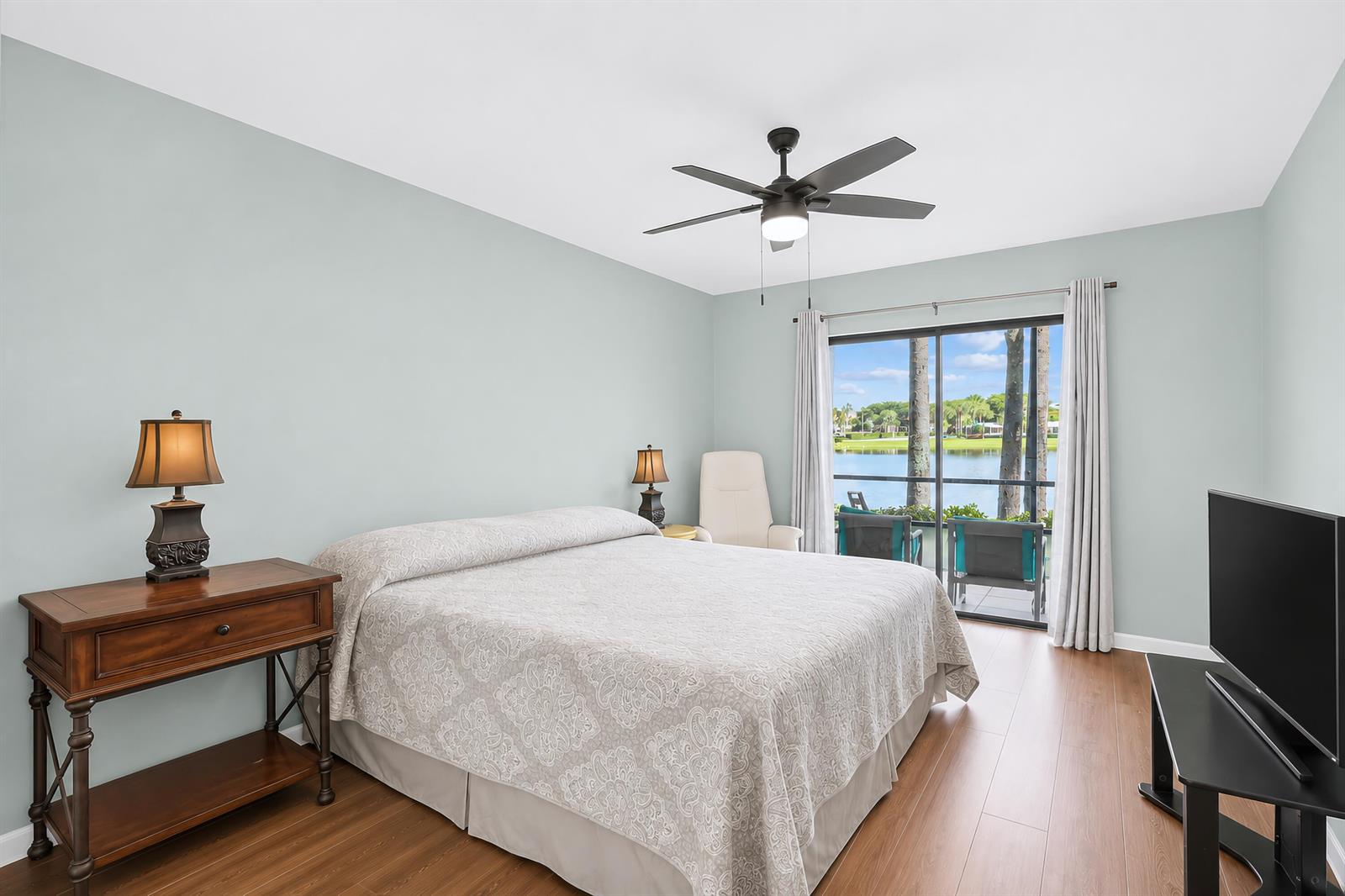 A bedroom with light blue walls, a bed, a wooden console table, and a sliding door — 7892 Willow Springs Drive # 1517, FL 33467, FL